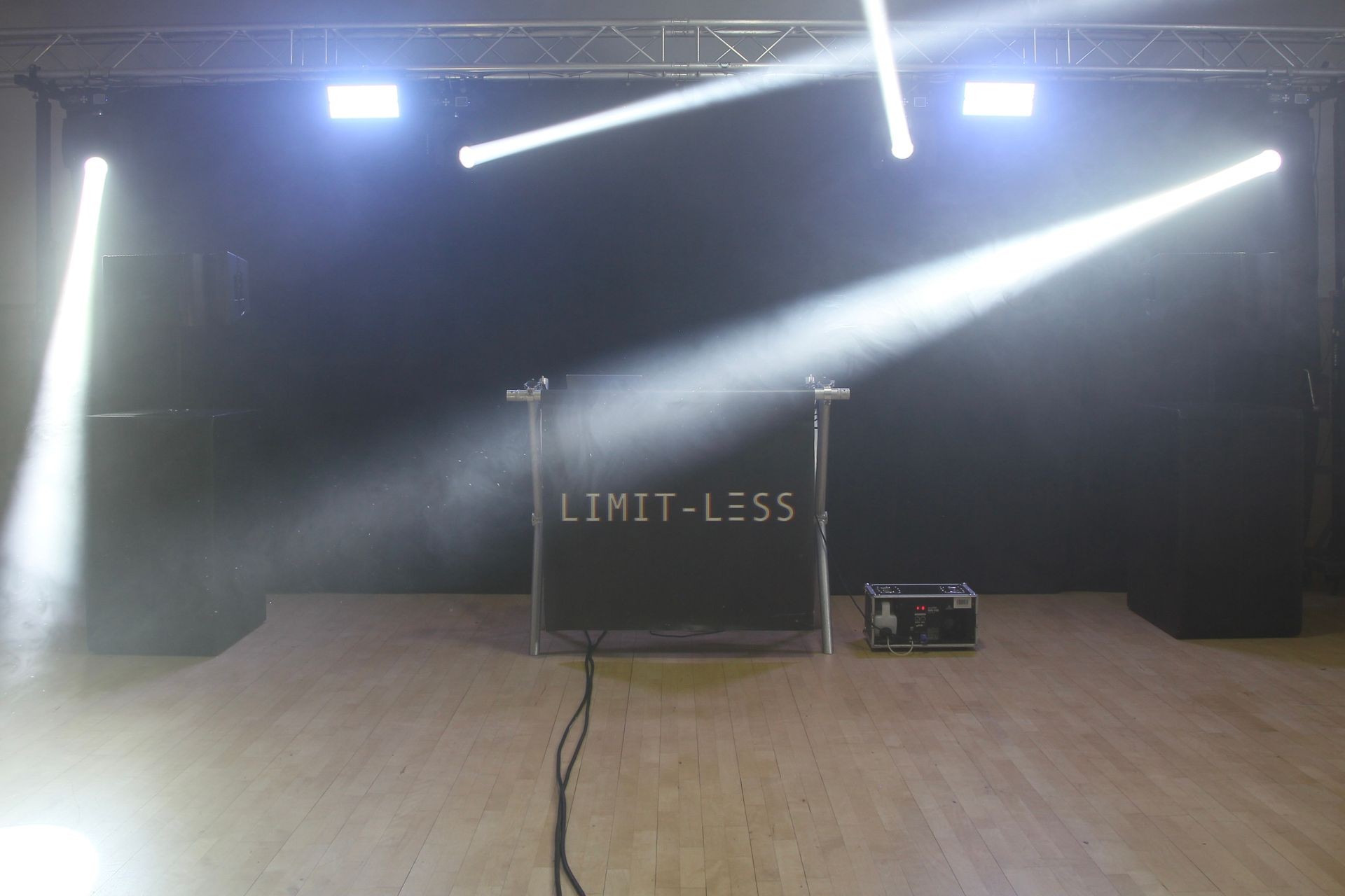 Stage with black backdrop, spotlights, and 'LIMIT-LESS' written on a panel.